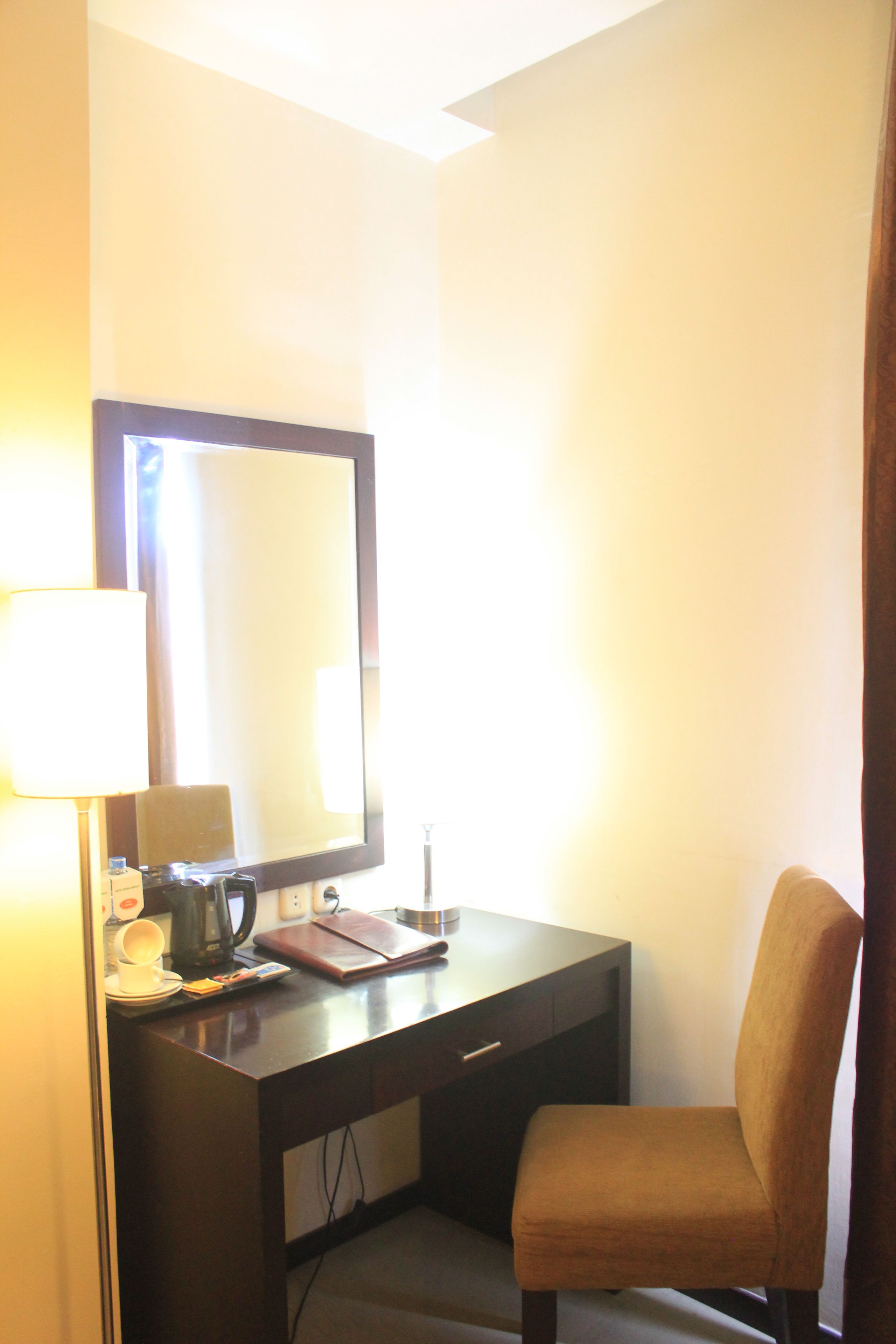 A hotel room with a desk, chair, lamp, and a large mirror.