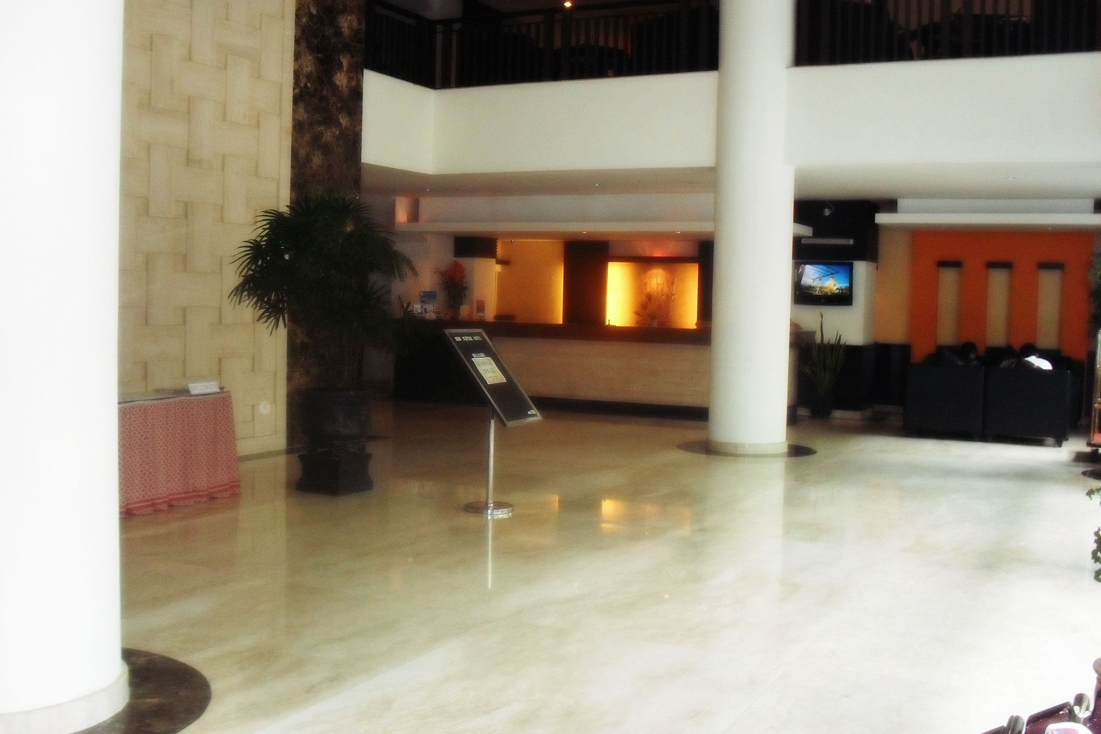 A lobby with a reception desk, a large potted plant, and a signboard.