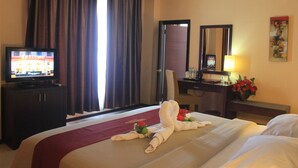 Una habitación de hotel con cama, televisión sobre un mueble, escritorio con lámpara y espejo.
