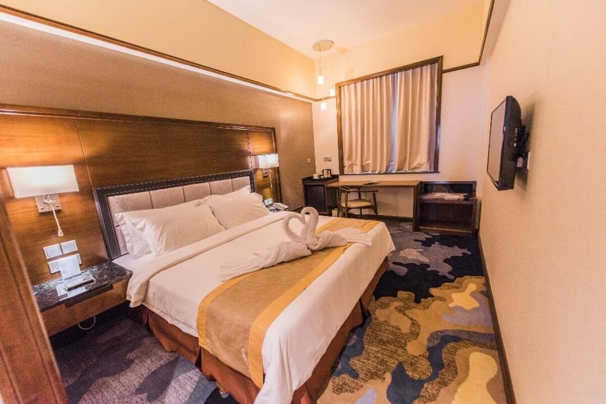 A hotel room with a large bed, a desk, a chair, a TV, and a window with curtains.