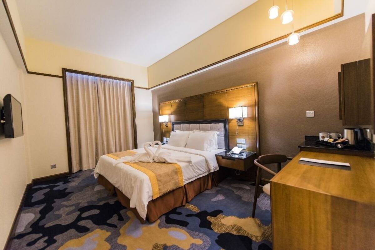 A hotel room with a large bed, a desk, a chair, and a nightstand.