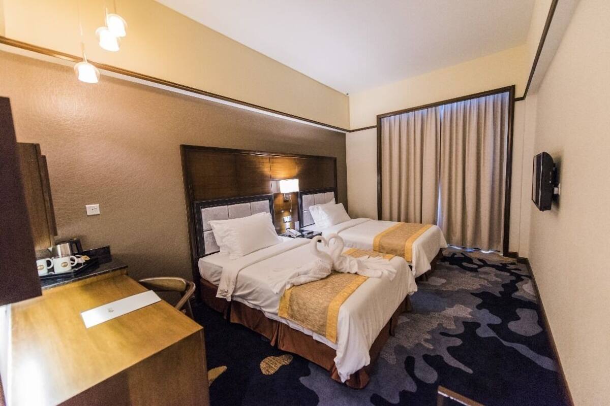 A hotel room with two beds, a desk, a chair, a TV, and a window with curtains.