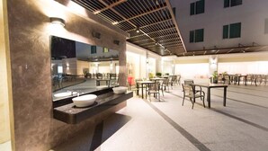 A modern outdoor seating area with tables and chairs, a large mirror, and a counter with a sink. - Nu Hotel (Bintulu)
