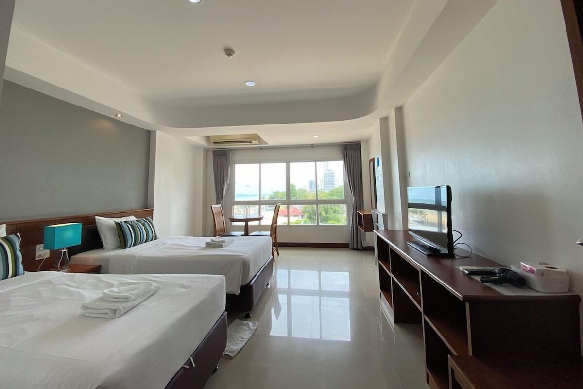 A hotel room with two beds, a TV, a desk, and a window with a view.