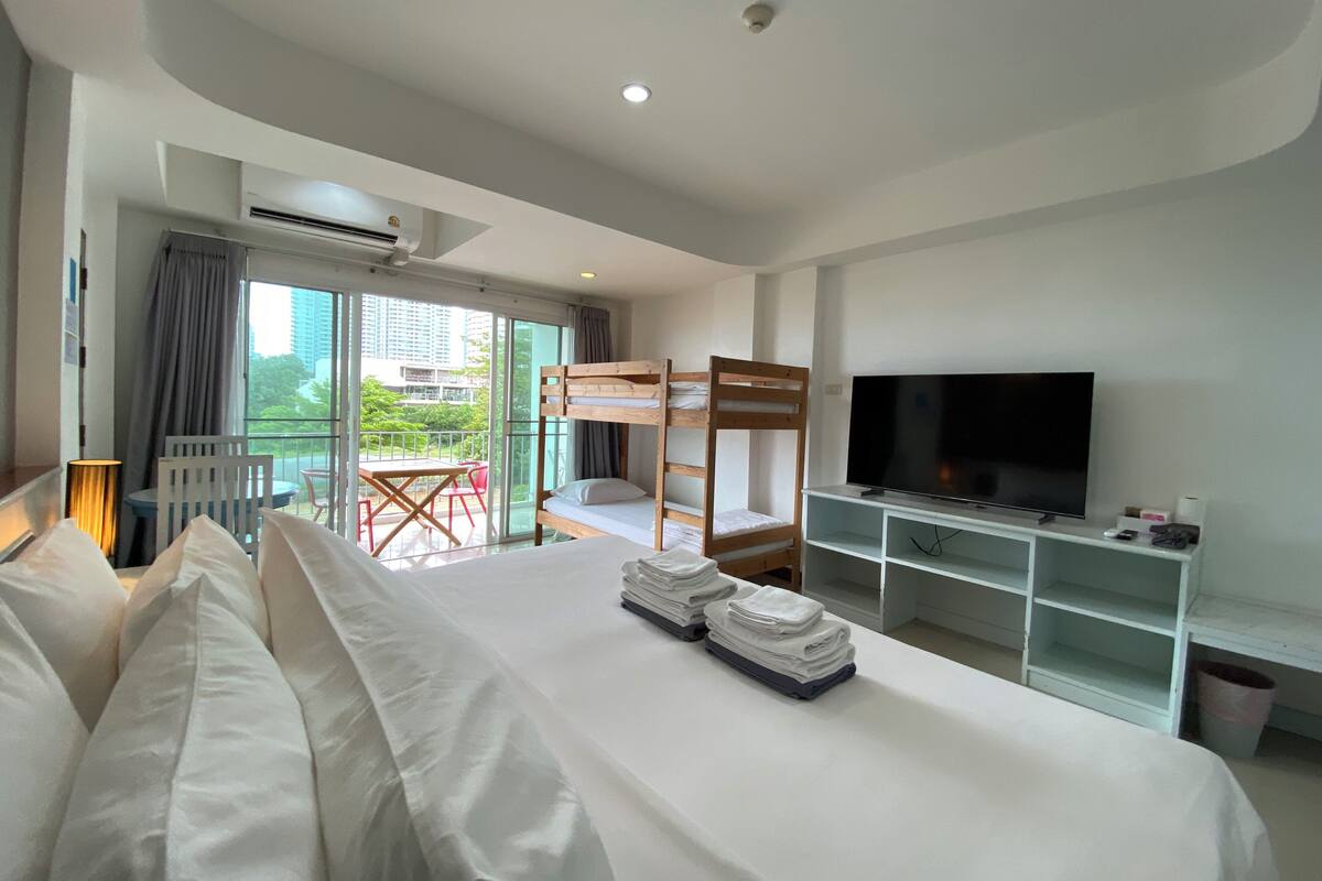 A hotel room with a bunk bed, a TV, a desk with a lamp, and a balcony with a view of the city.