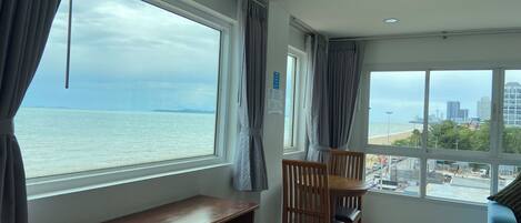 A room with a large window offering a view of the sea and a cityscape. There is a wooden table and two chairs.