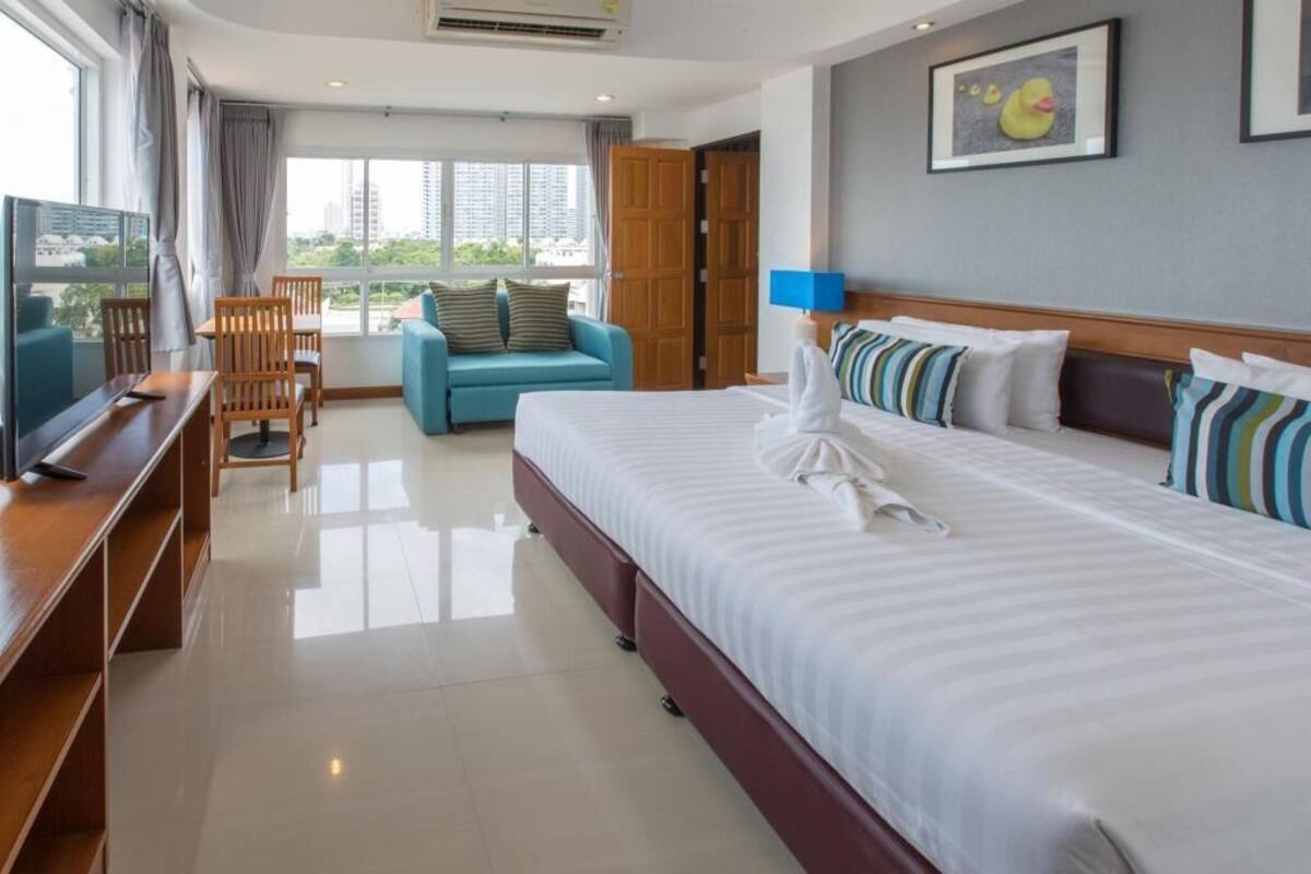 A hotel room with a bed, a desk, a chair, a sofa, a TV, and a window with a view of buildings.