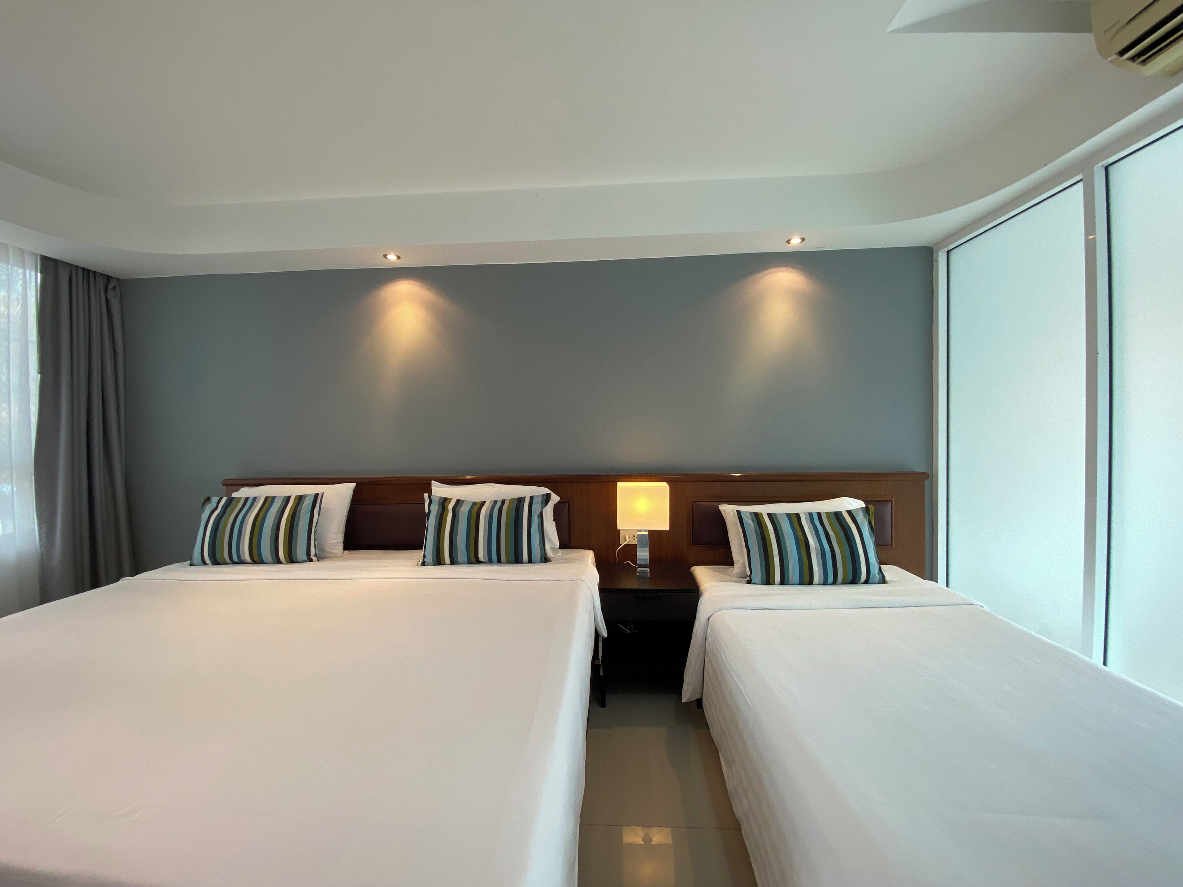 A hotel room with two beds, a nightstand, a lamp, and a large window.