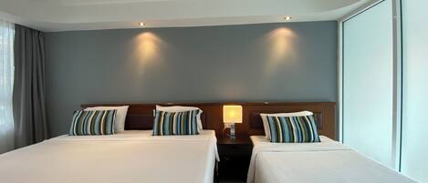 A hotel room with two beds, a nightstand, a lamp, and a large window.