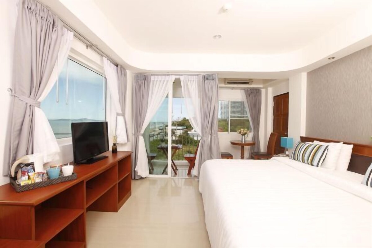 A hotel room with a bed, TV, and a balcony with a view.