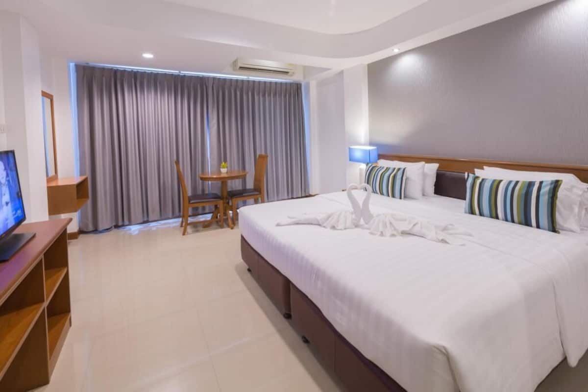 A hotel room with a large bed, a TV, a desk, and a window with curtains.