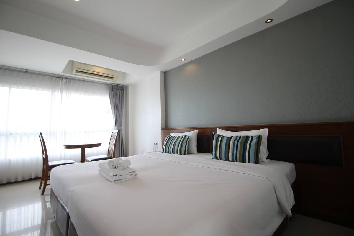 A hotel room with a large bed, a bedside table, a chair, and a window with curtains.