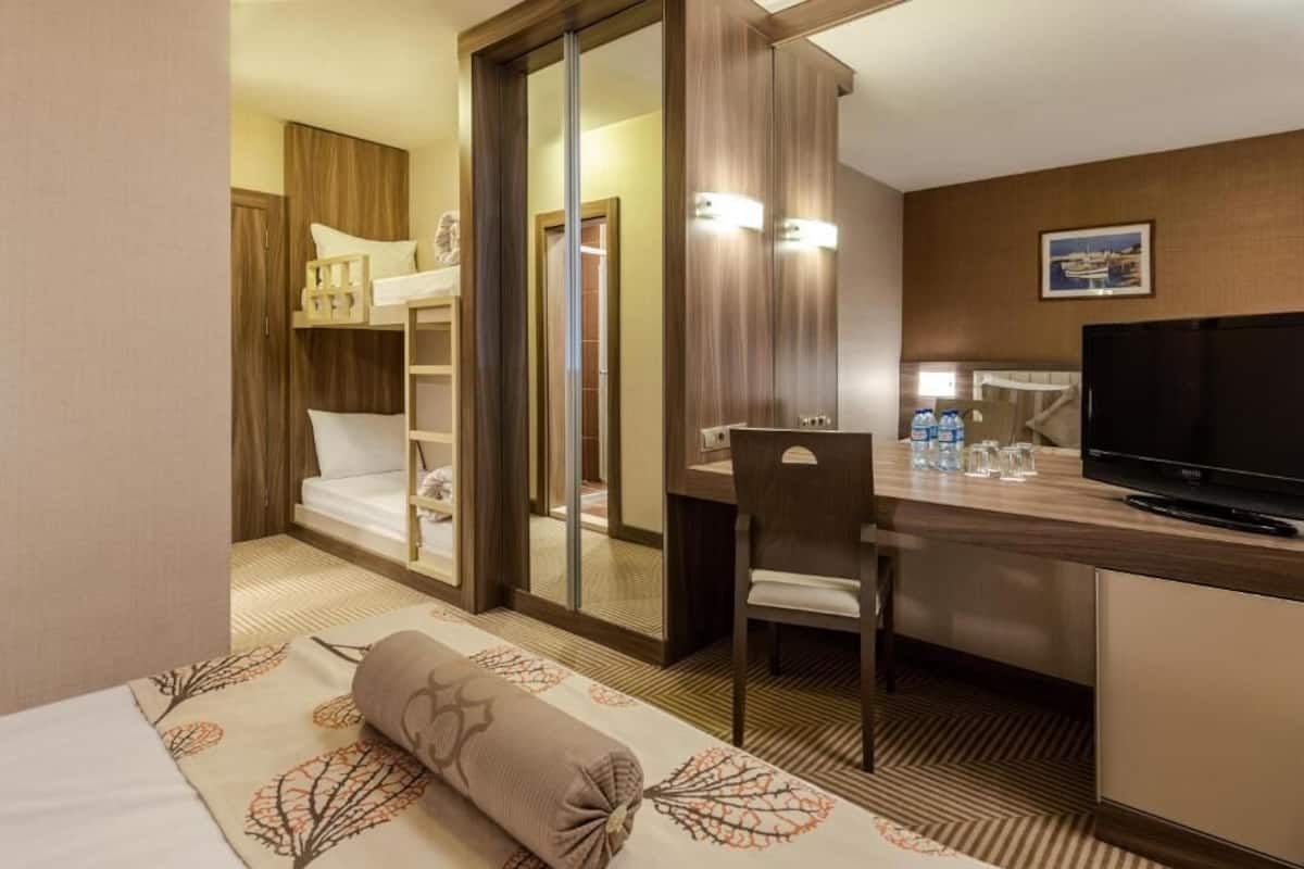 Une chambre d’hôtel avec un lit superposé, un bureau avec une chaise, une télévision et une salle de bain avec douche et toilettes.