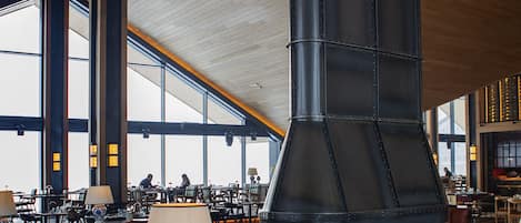 A spacious interior with a large fireplace, wooden furniture, and large windows providing natural light.