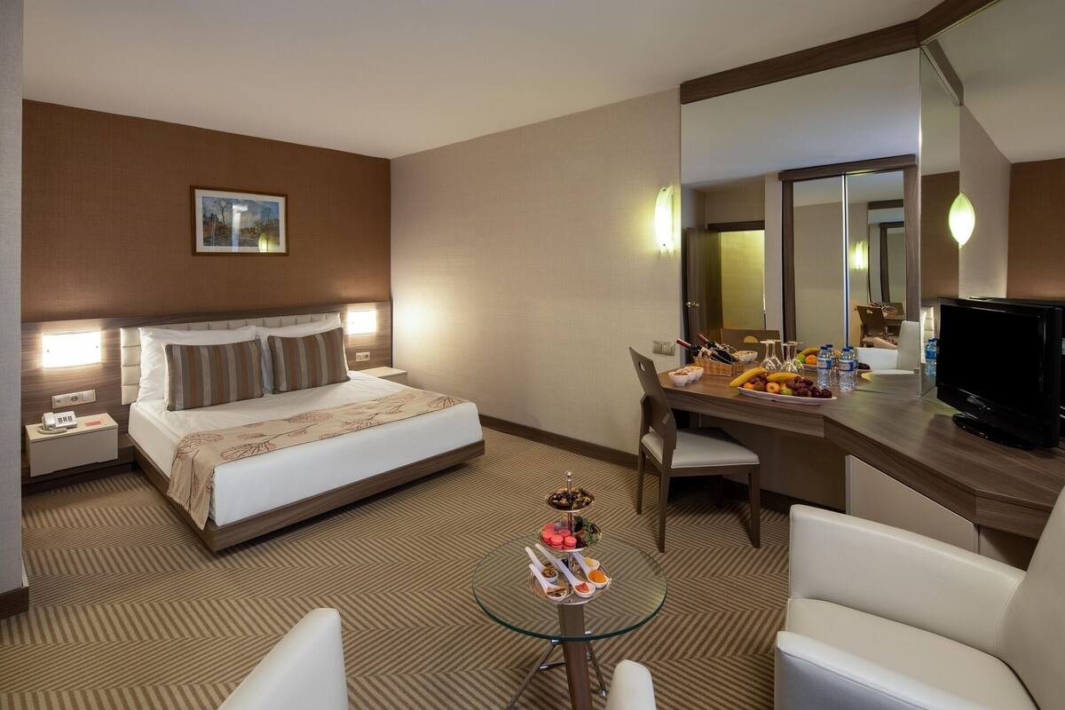 Une chambre d’hôtel comprenant un lit, une table de chevet, un bureau, une chaise et une petite table en verre avec des collations.