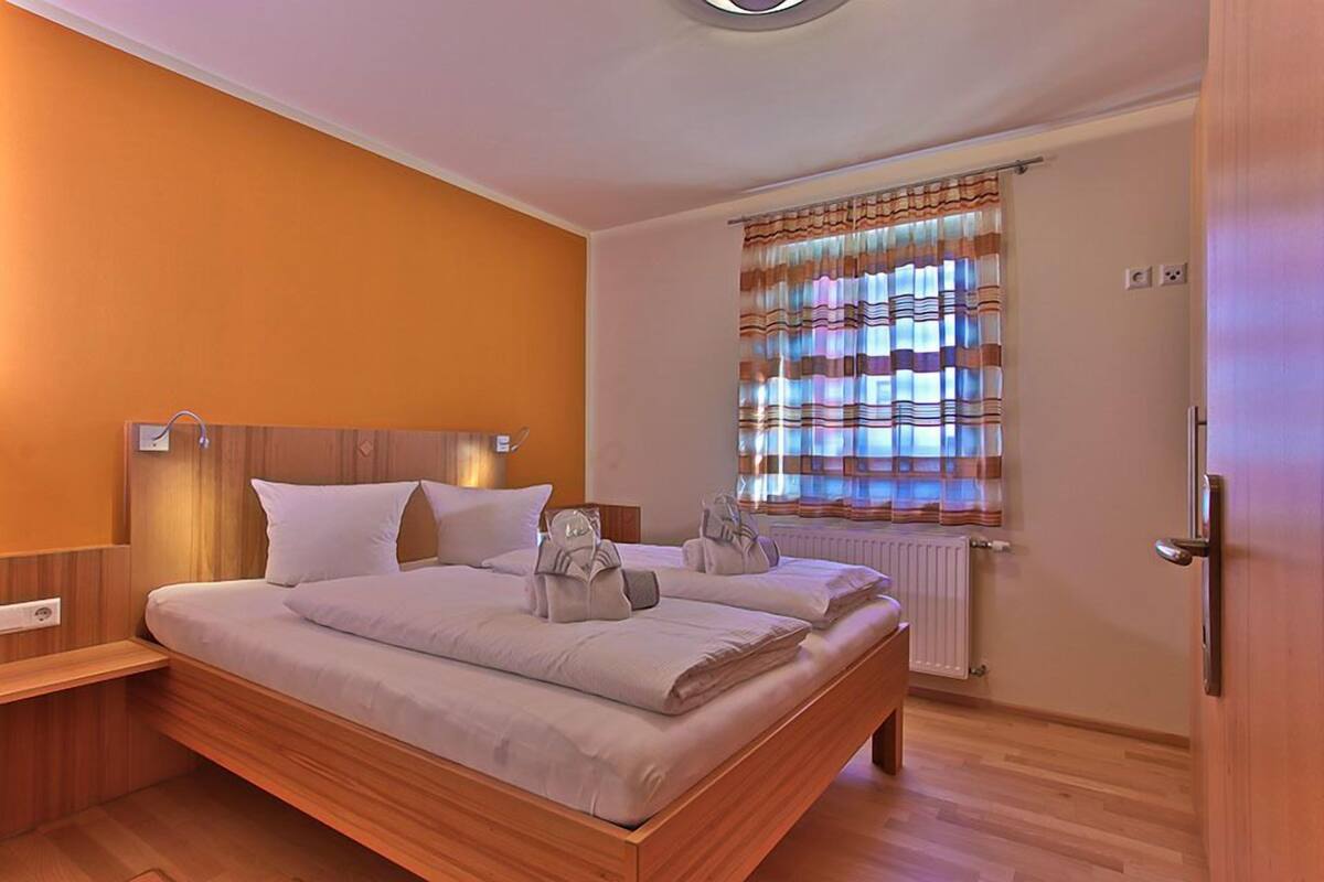 A bedroom with a wooden bed, a bedside table, a window with striped curtains, and a radiator.