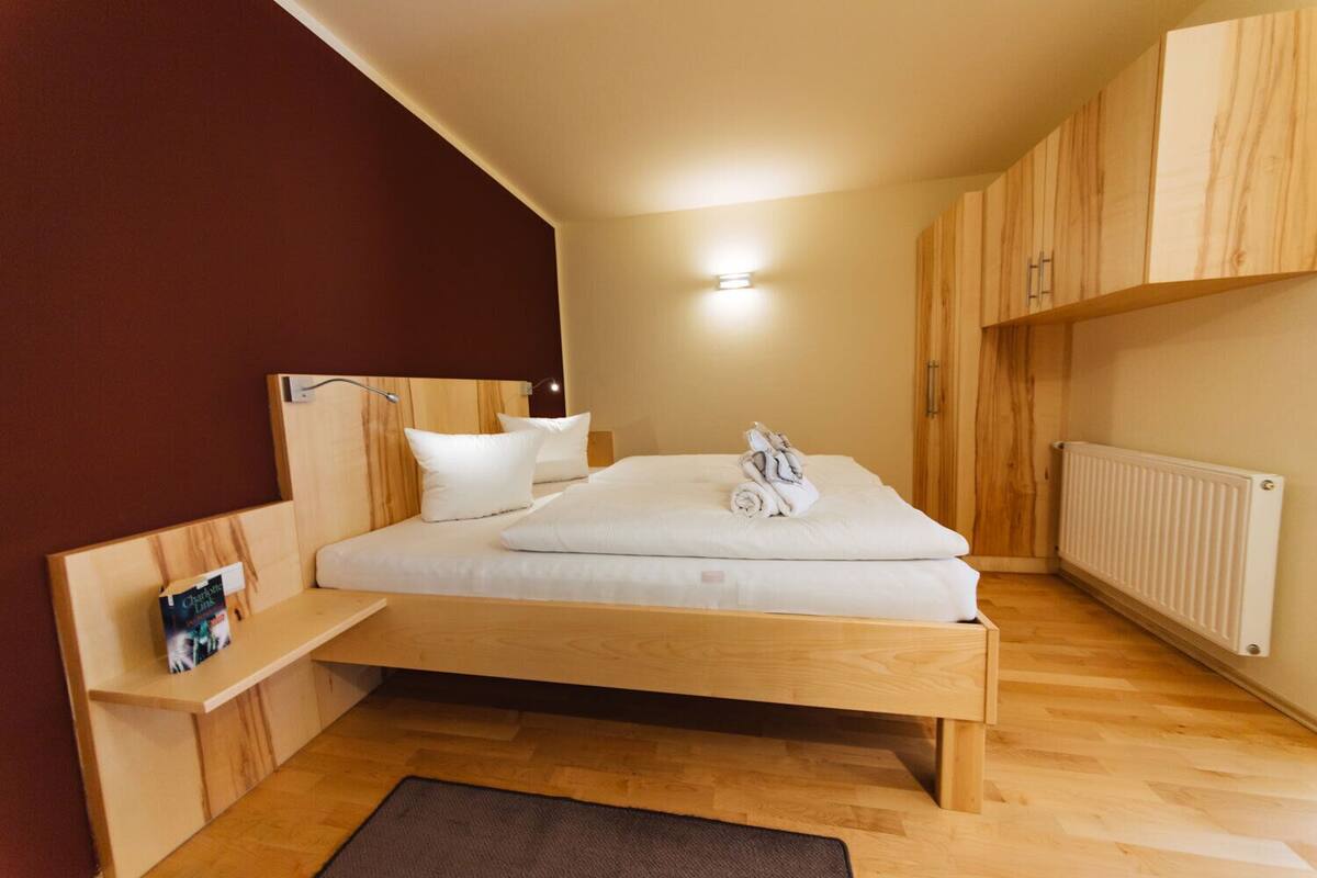 A bedroom with a wooden bed, a nightstand, a wall-mounted shelf, and a radiator.