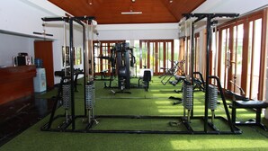 A gym with various exercise equipment, a reception desk, and large windows allowing natural light. - Mutiara Hotel Cilacap (Cilacap)