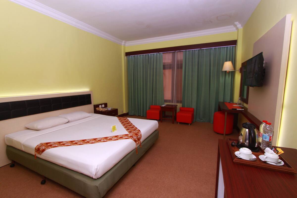 Habitación de hotel con cama, escritorio, silla, televisión y bandeja con tetera y tazas.