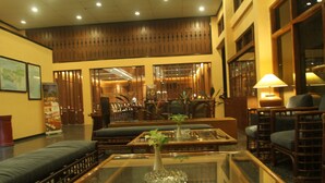 A lobby with a seating area, a glass coffee table with a plant, and a wooden reception desk. - Mutiara Hotel Cilacap (Cilacap)