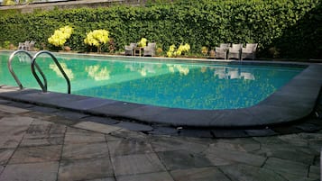 Une piscine entourée d’une terrasse dallée de pierres, de verdure luxuriante et de fauteuils de jardin en osier.