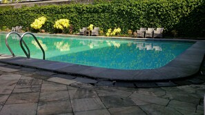 A swimming pool with a stone-tiled deck, surrounded by lush greenery and wicker lounge chairs. - Mutiara Hotel Cilacap (Cilacap)