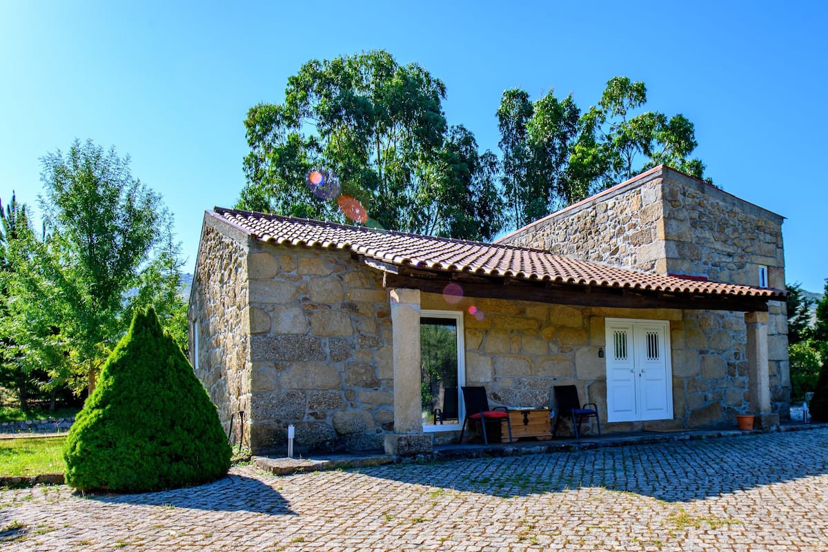 Ein Steinhaus mit einem Ziegeldach, einer Holztür und einer kleinen Veranda mit einer Bank und einem Tisch.