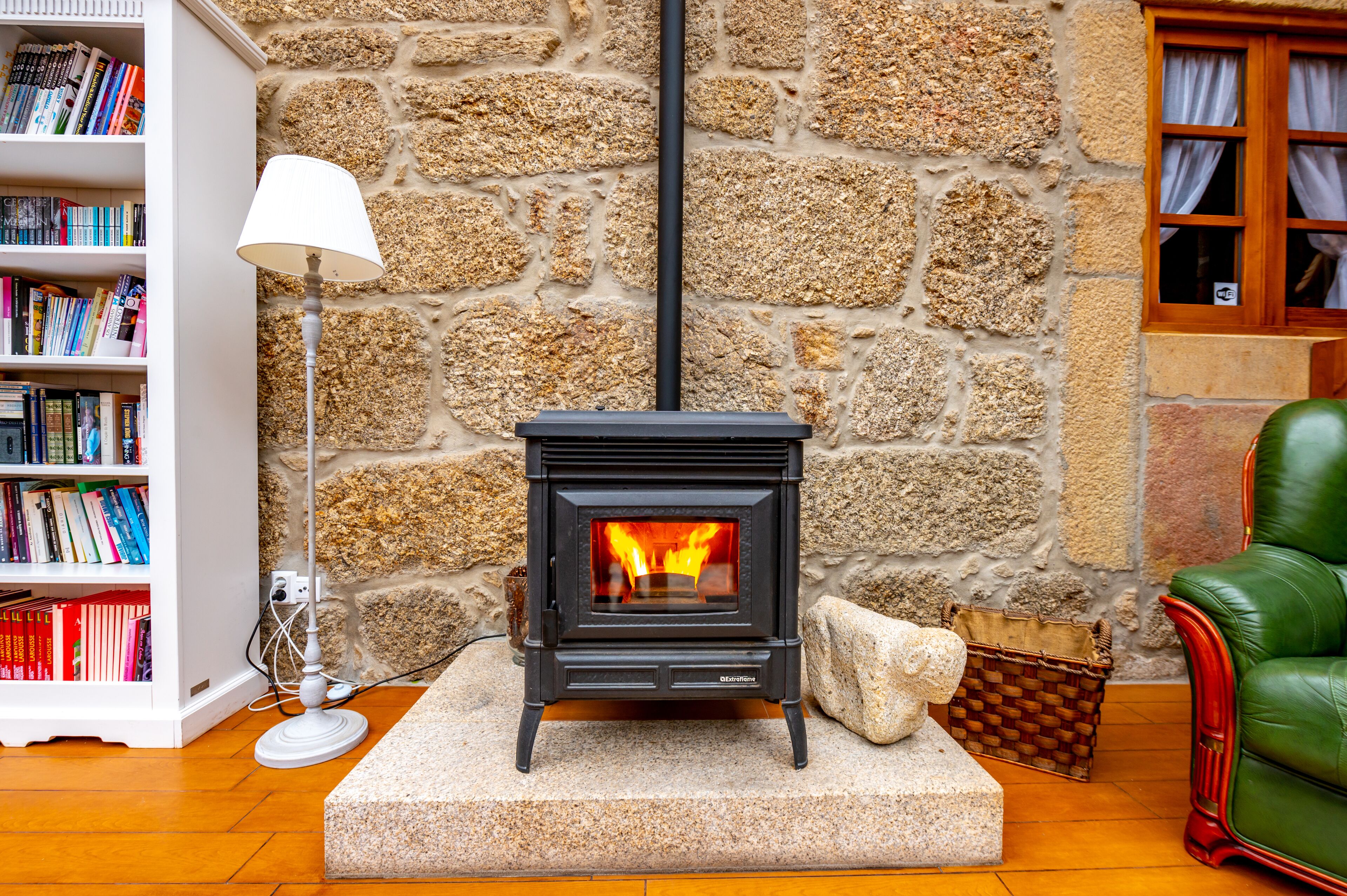 A cozy room with a stone wall, a fireplace, a bookshelf, a lamp, and a green leather chair.