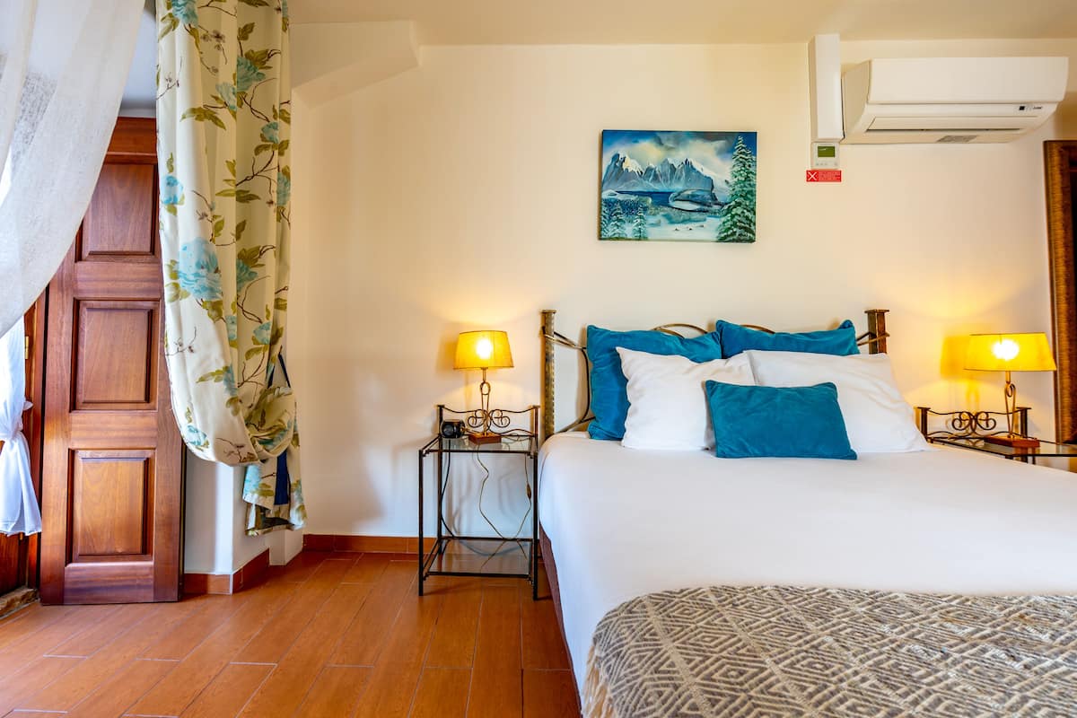 Ein Hotelzimmer mit einem Bett, zwei Nachttischen mit Lampen, einem Bild an der Wand und einer Klimaanlage.