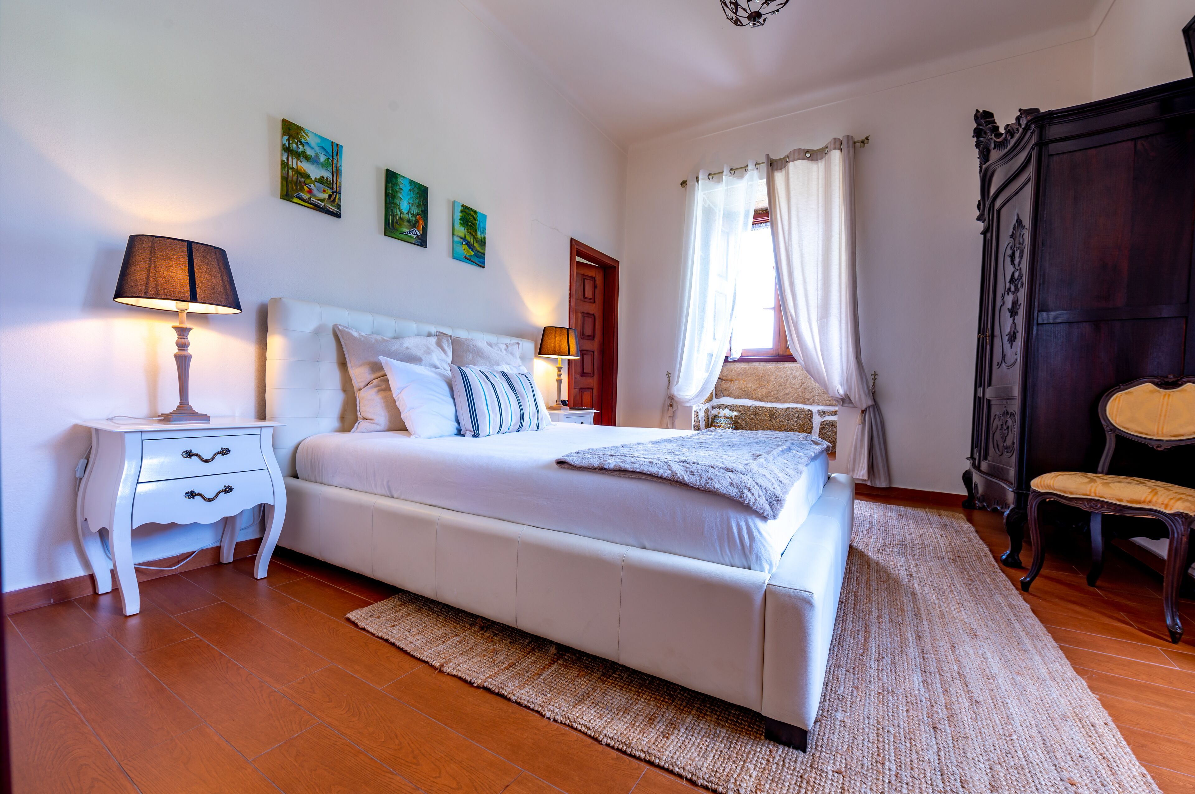 A bedroom with a large bed, a nightstand, a chair, and a wardrobe.