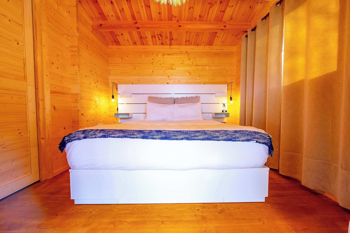 Ein Zimmer mit Holzwänden, einem großen Bett, Holzboden und einer geneigten Decke.