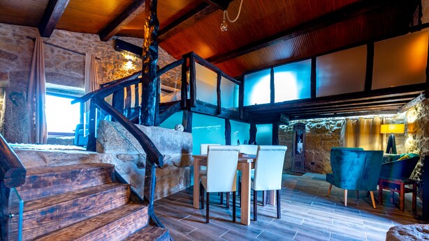 A rustic interior with a stone staircase, wooden flooring, and a dining area with chairs and a table.