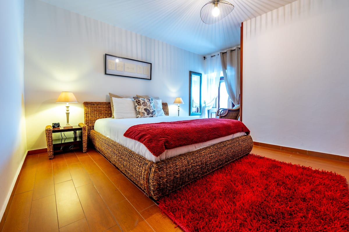 Ein Schlafzimmer mit einem großen Bett, zwei Nachttischen, einem roten Teppich und einer Deckenleuchte.