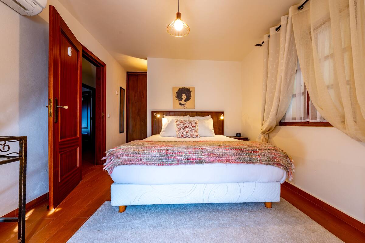 Ein Schlafzimmer mit einem großen Bett, einem hölzernen Kopfteil, einem Nachttisch und einer Pendelleuchte.
