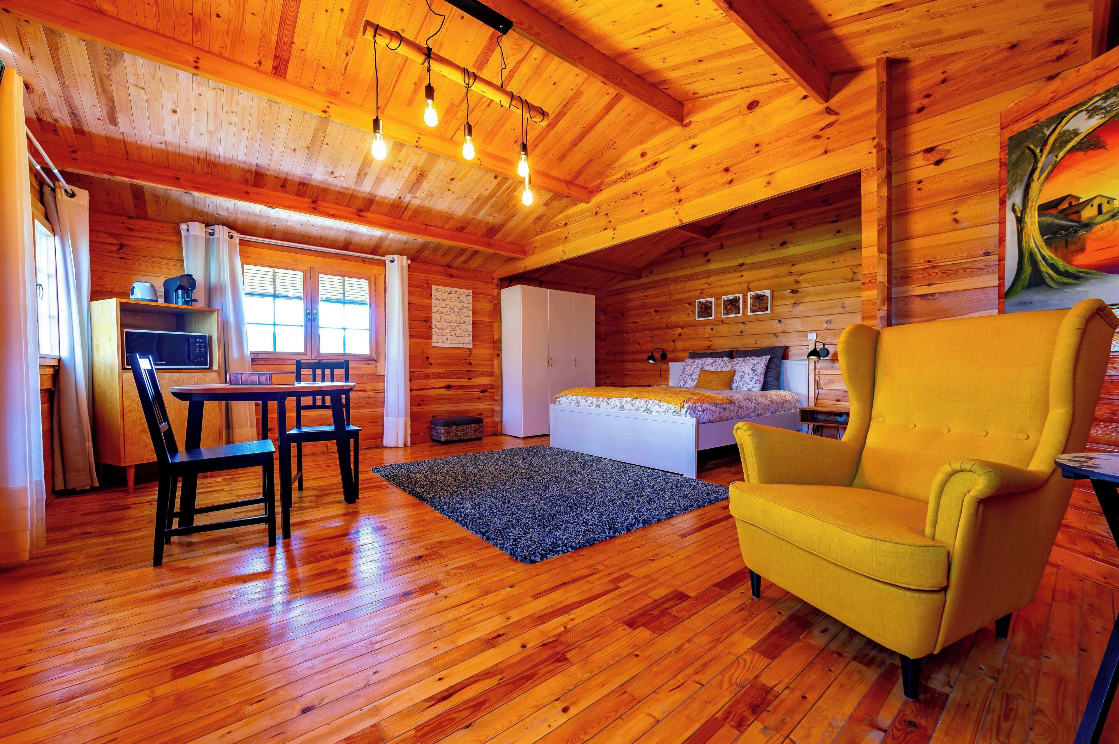 A wooden cabin with a dining area, a bed, and a yellow armchair.
