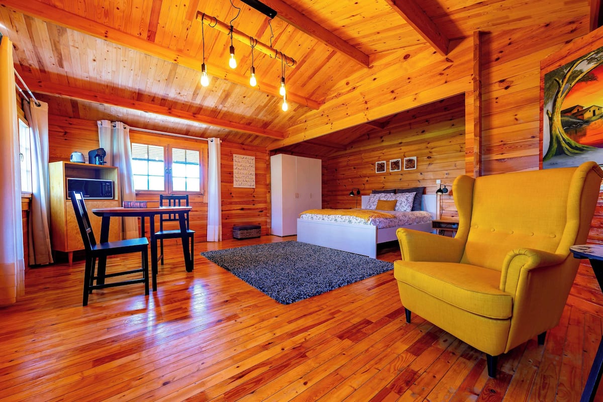 Eine Holzhütte mit Essbereich, einem Bett und einem gelben Sessel.