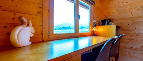 L’intérieur d’un chalet en bois, avec un comptoir en bois, deux chaises, un objet décoratif et une fenêtre donnant sur un paysage enneigé.