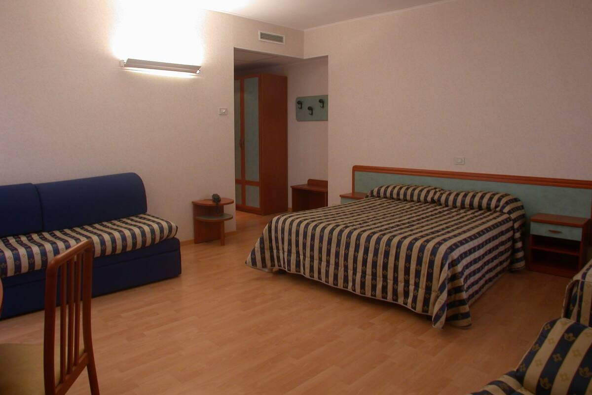 Ein Schlafzimmer mit einem Bett, einem blauen Sofa, einem Holzstuhl und einem kleinen Tisch.