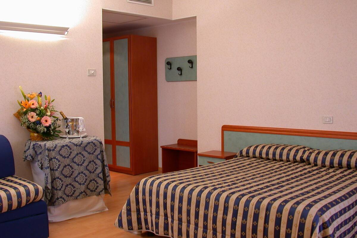 Ein Hotelzimmer mit einem Bett, einem kleinen Tisch mit Blumenvase, einem Sessel und einem Kleiderschrank.