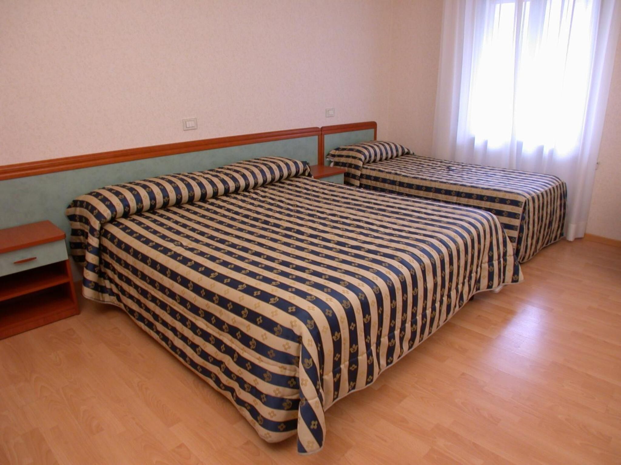A hotel room with two beds, wooden flooring, and a window with curtains.