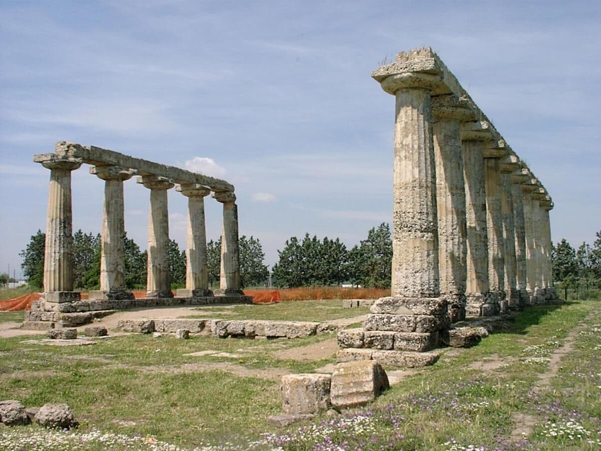 Ancient stone columns and ruins in a grassy field.