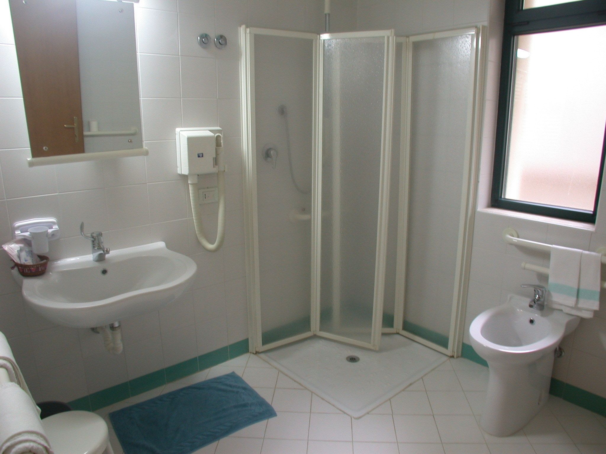 A bathroom with a shower enclosure, a sink, a bidet, and a toilet.