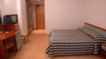 Un dormitorio con cama, un escritorio con televisor y una silla.