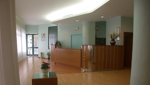 A reception area with a wooden reception desk, a potted plant, and a clock on the wall. - Hotel La Pergola (Rionero in Vulture)