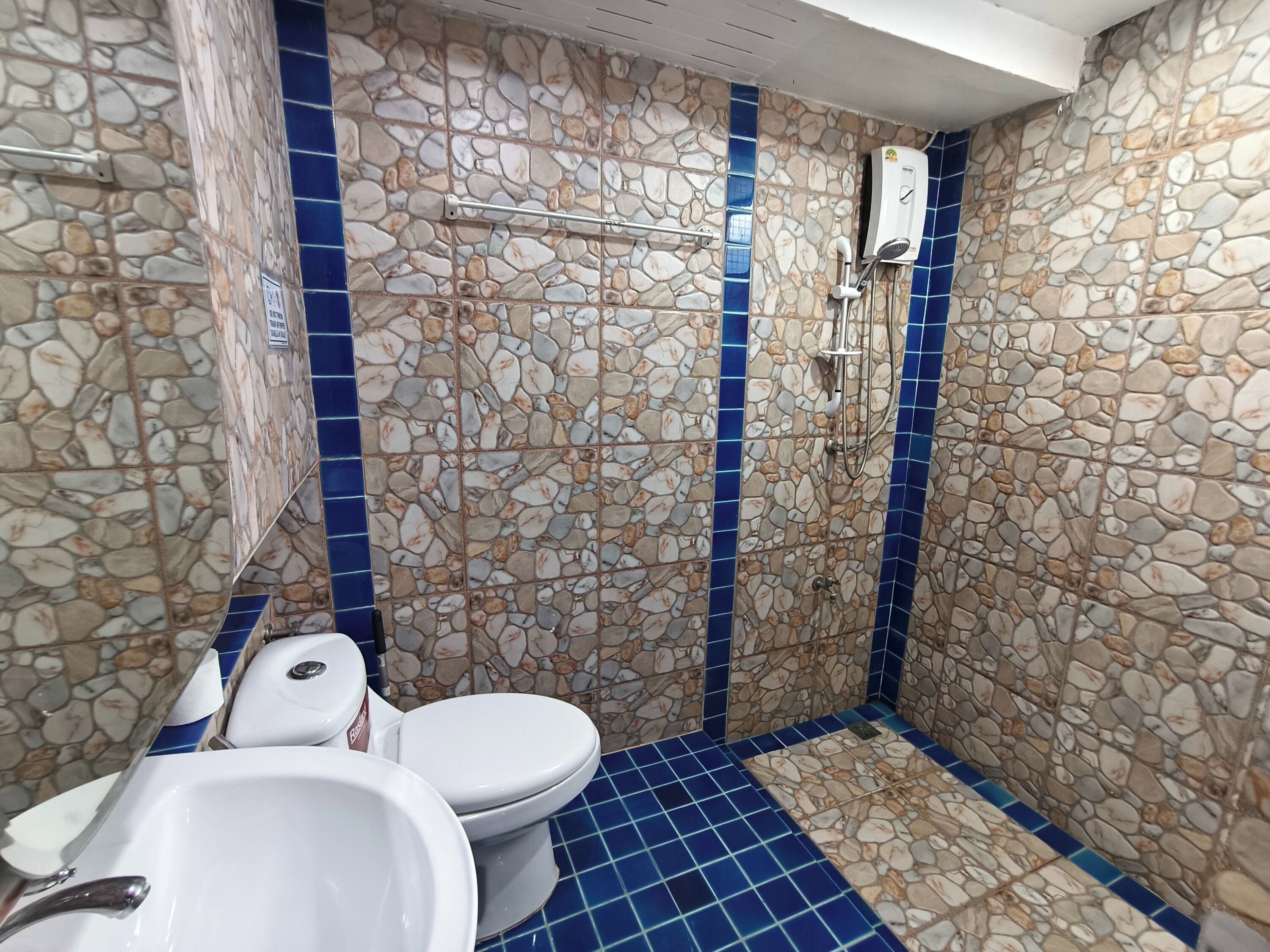 A bathroom with a stone mosaic wall, a blue-tiled floor, a toilet, and a sink.