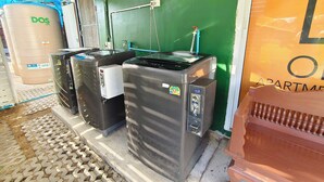 Un dispensador de agua, un tanque de agua grande y un banco de madera frente a un edificio.