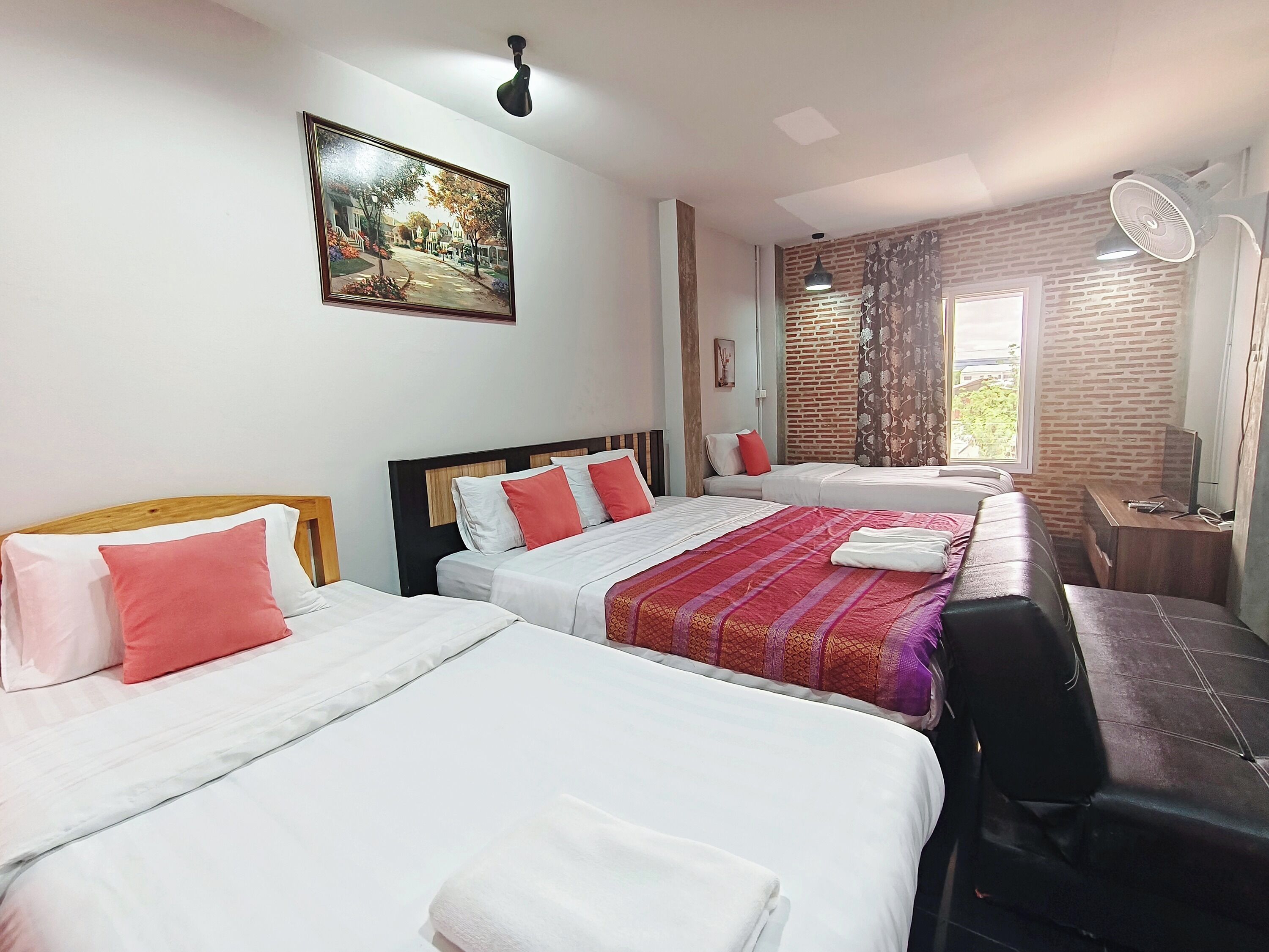 A hotel room with three beds, a desk, a chair, a window with curtains, and a painting on the wall.
