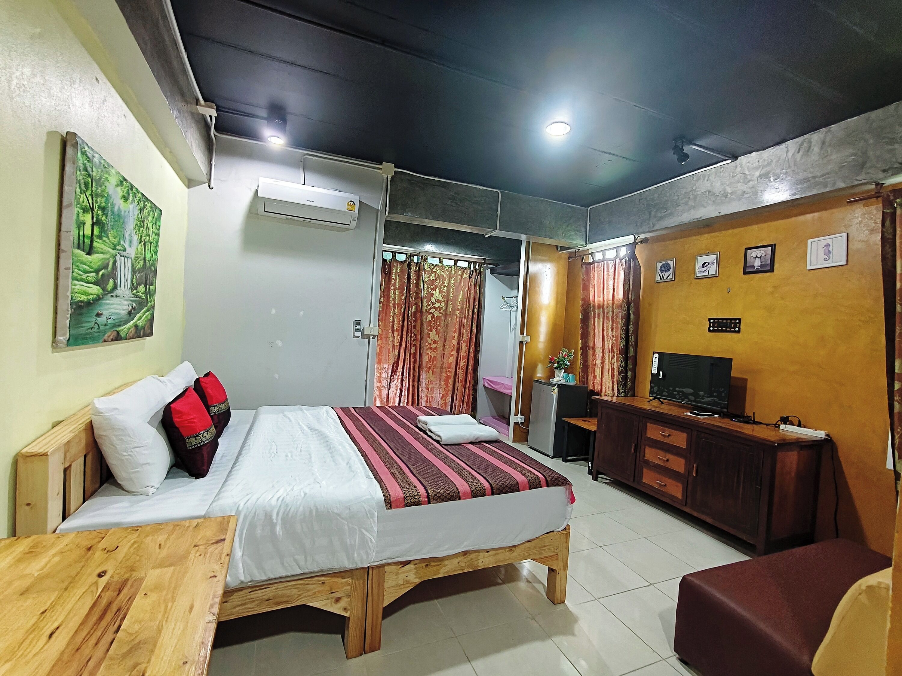 A room with a bed, a desk, a TV, and a painting on the wall.