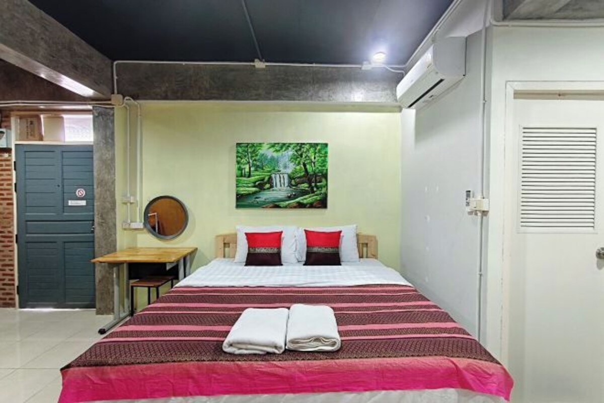 A bedroom with a bed, a painting, a desk, and a door.
