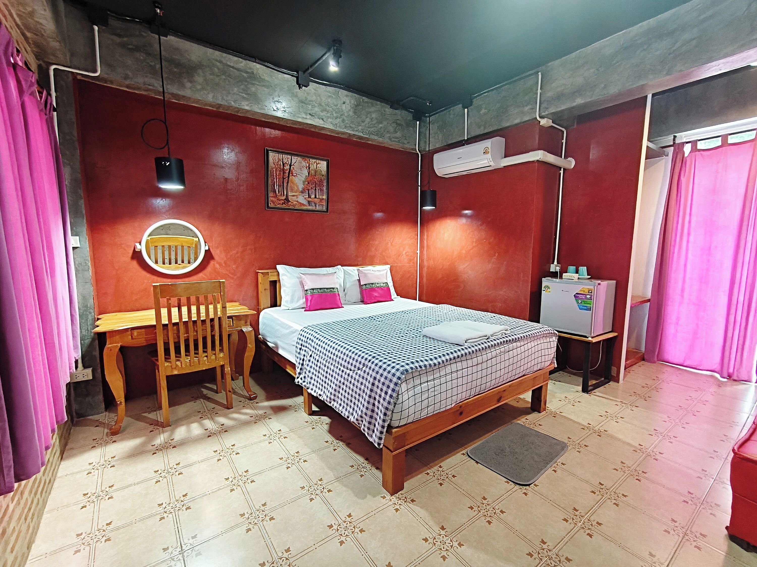 A bedroom with a bed, a desk, a chair, a mirror, an air conditioner, and a refrigerator.